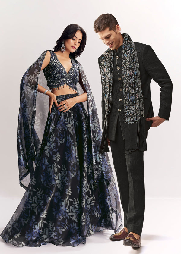 Elegant Festive Couple Set – Black Printed Mirror Work Lehenga Choli In Organza Tissue For Her And Black Matka Silk Jodhpuri Set With Mandarin Collar For Him